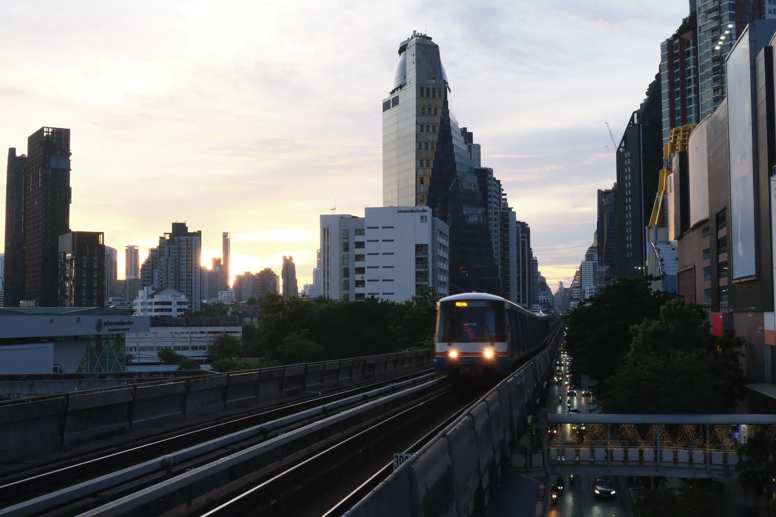 Auf dem Bild fährt am Abend ein BTS-Skytrain auf erhöhten Gleisen durch Bangkok.