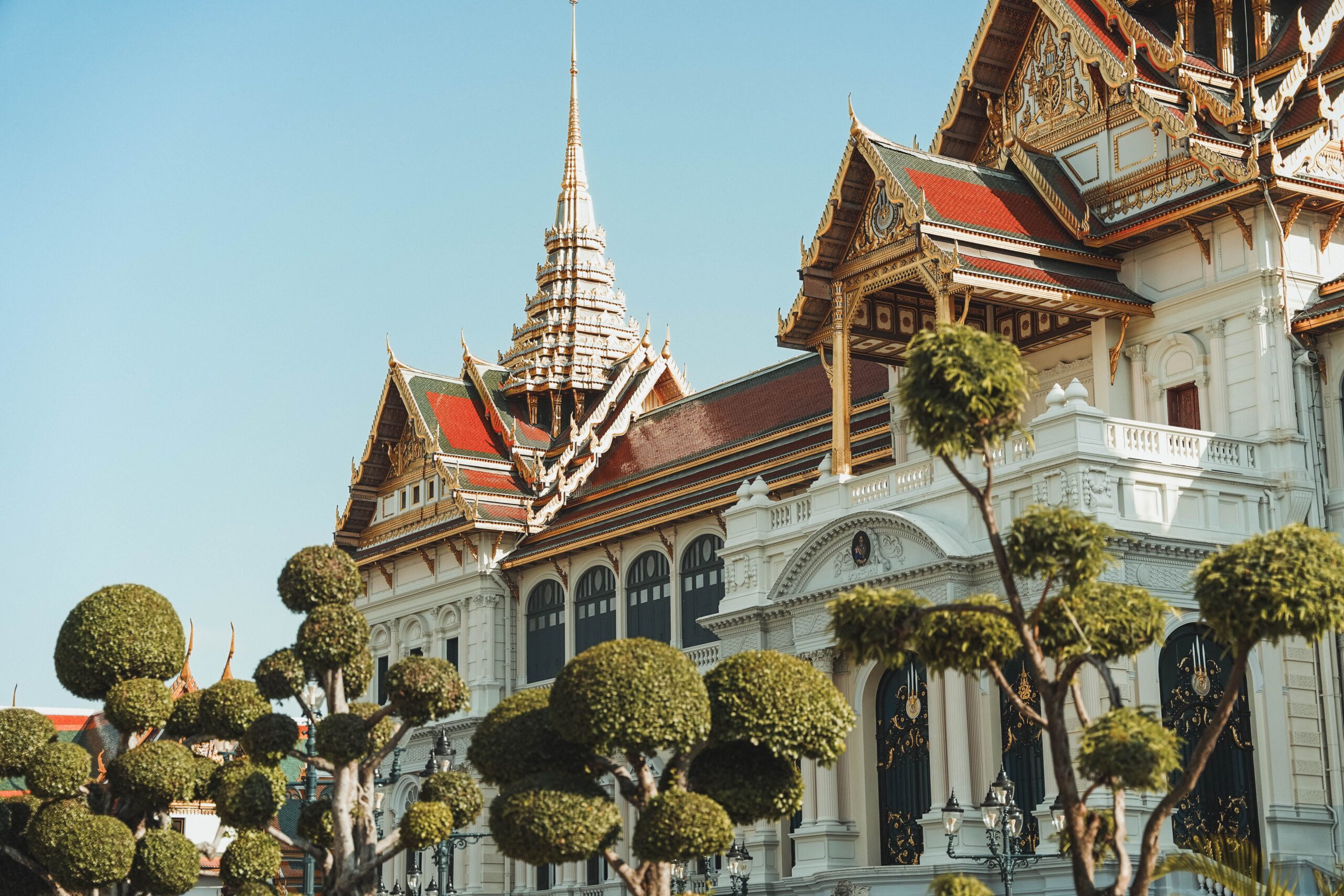 Auf dem Bild zum MRT-Plan für Bangkok ist die verzierte weiße Fassade des Großen Palasts unter blauem Himmel zu sehen.