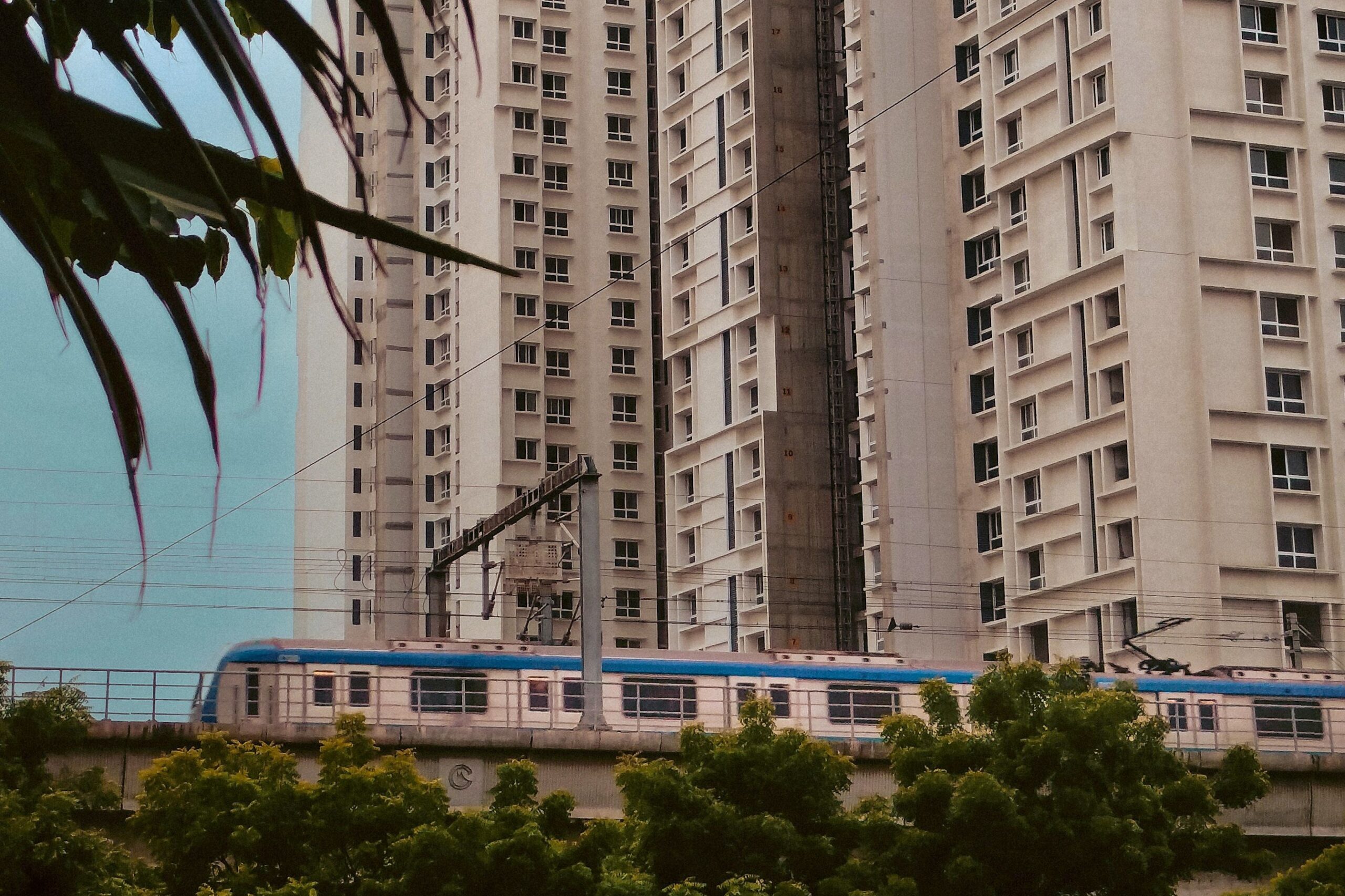 Ein Zug der Metro Chennai fährt auf einem Hochbahnviadukt vor Wohnhochhäusern.