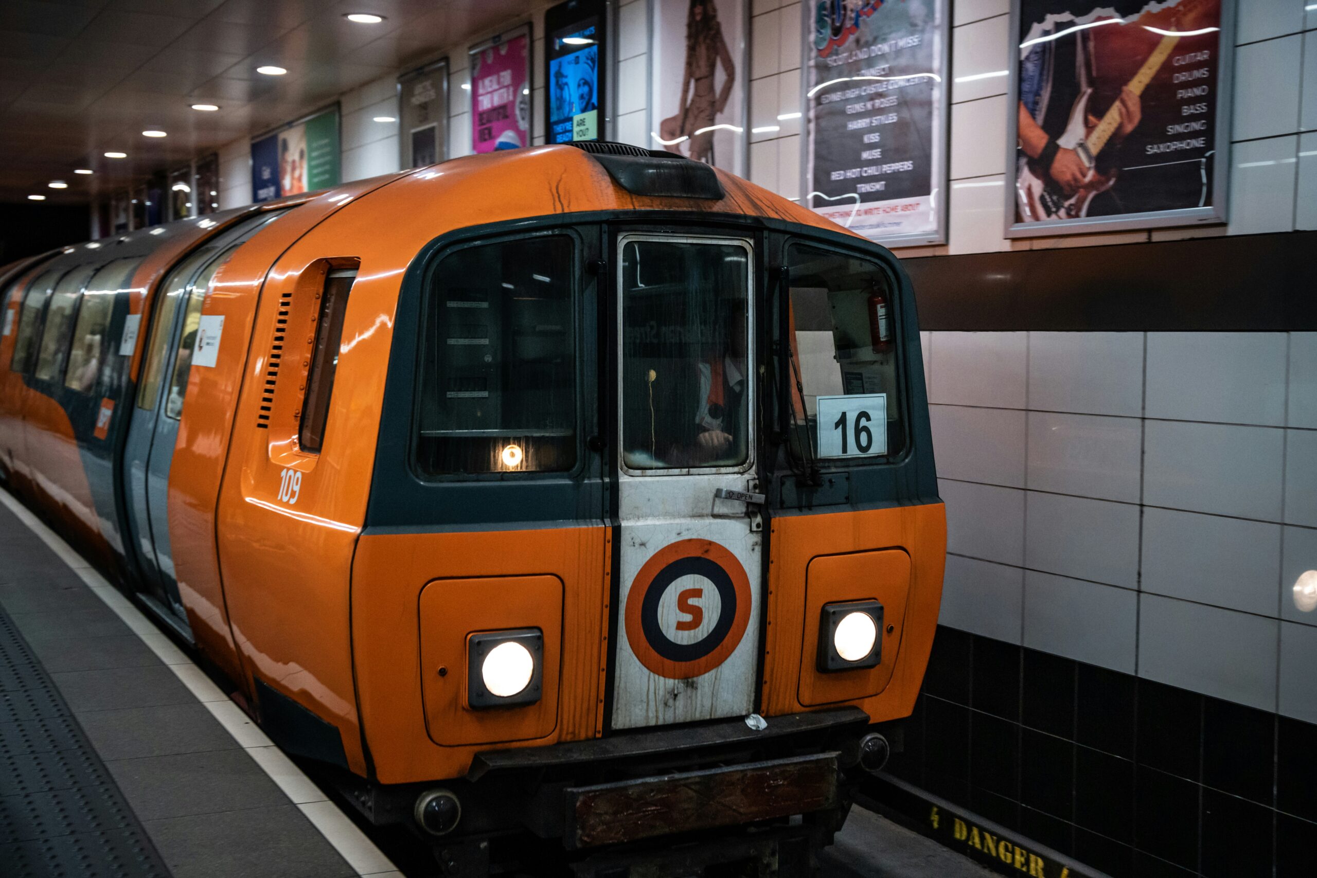 An einem Bahnsteig steht ein historischer orangefarbener Zug der U-Bahn in Glasgow.