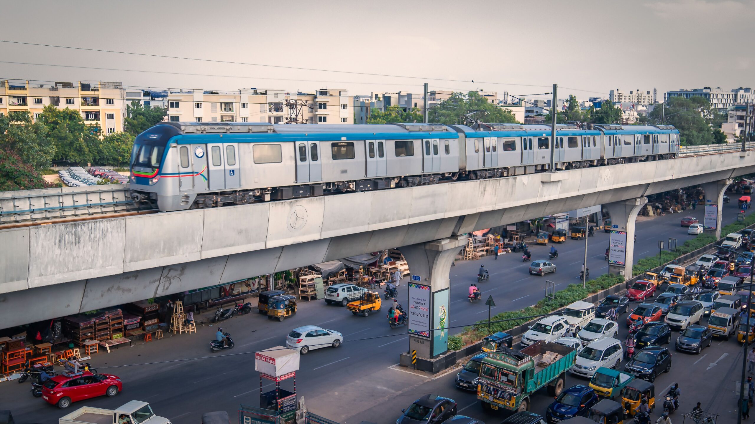 Ein Metrozug fährt im Streckennetz von Hyderabad auf einem Viadukt über eine belebte Straße.
