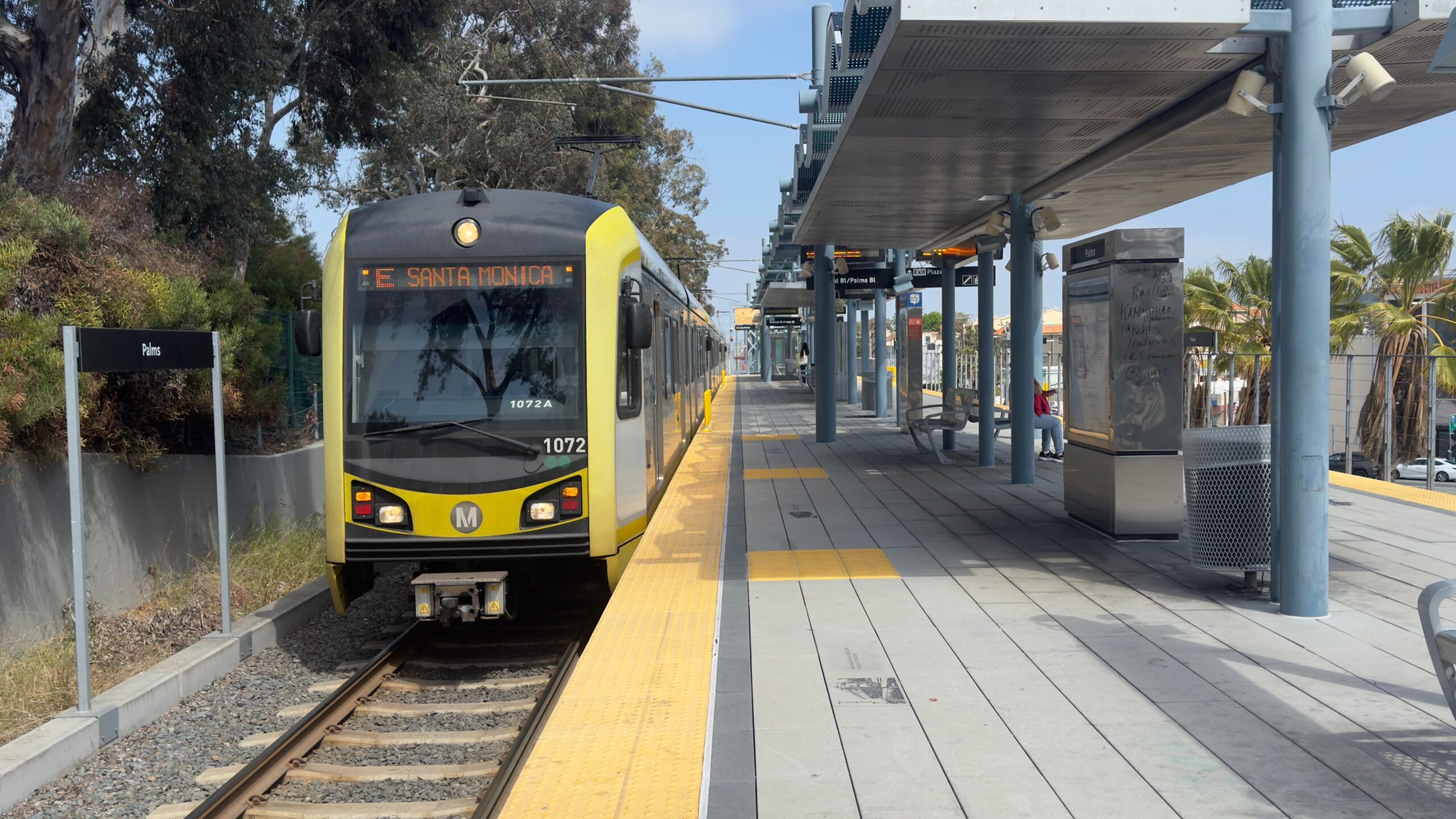 Ein gelber Zug der E Line hält an der Station Palms; auf der LA Metro Map ist sein Ziel Santa Monica verzeichnet.