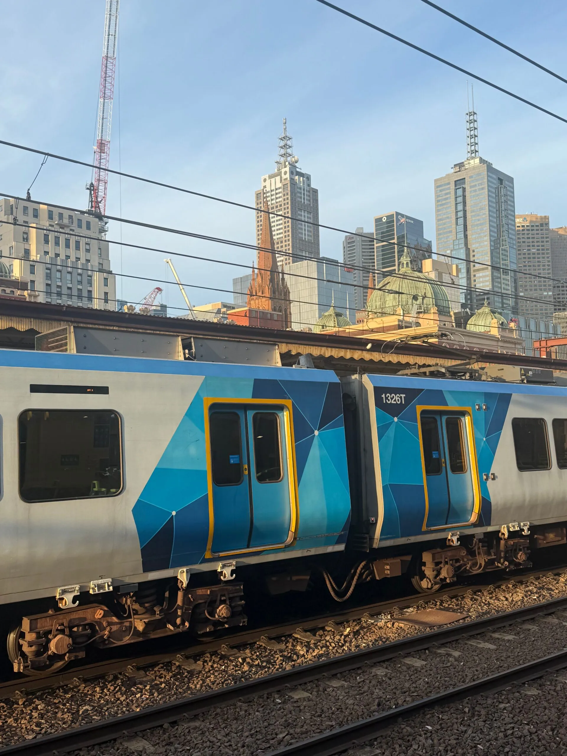 A Metro Trains Melbourne suburban train passes Flinders Street Station beneath the central city skyline.