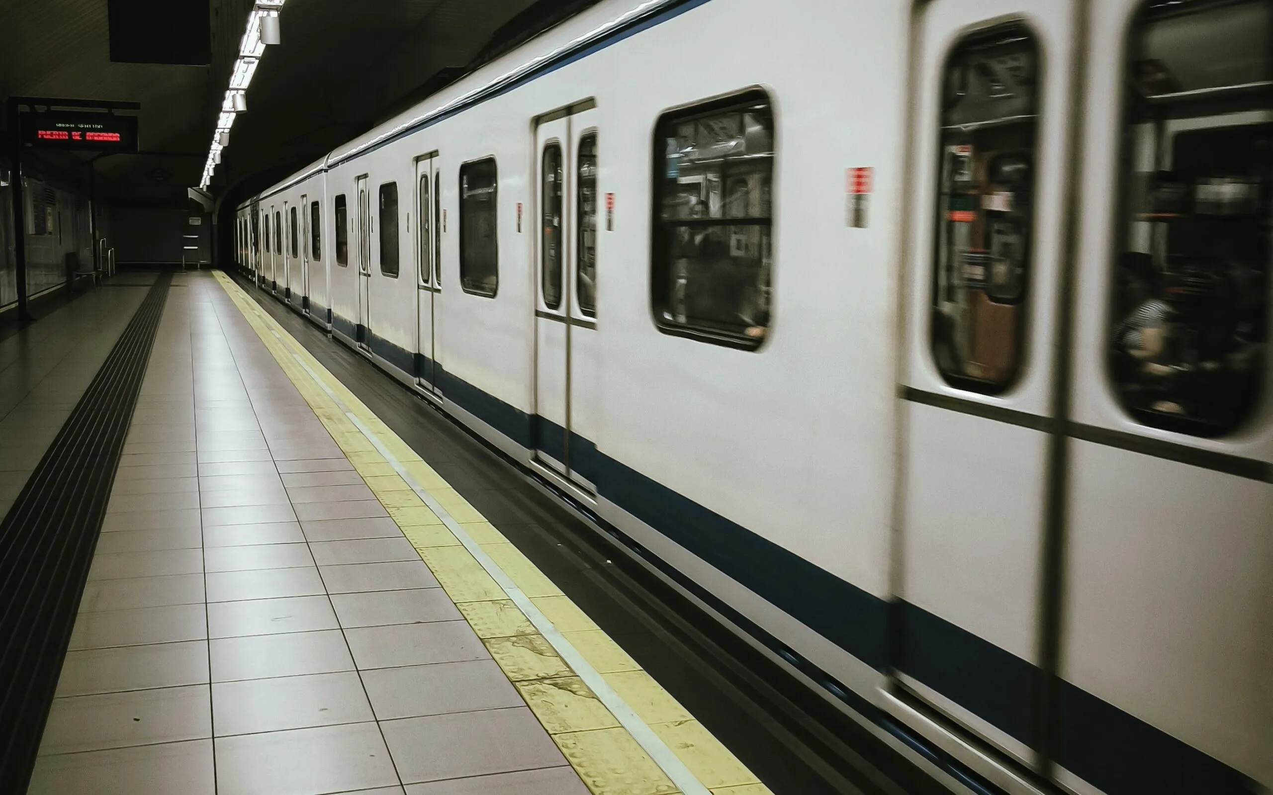 The image shows a Madrid Metro train stopped at an underground platform.