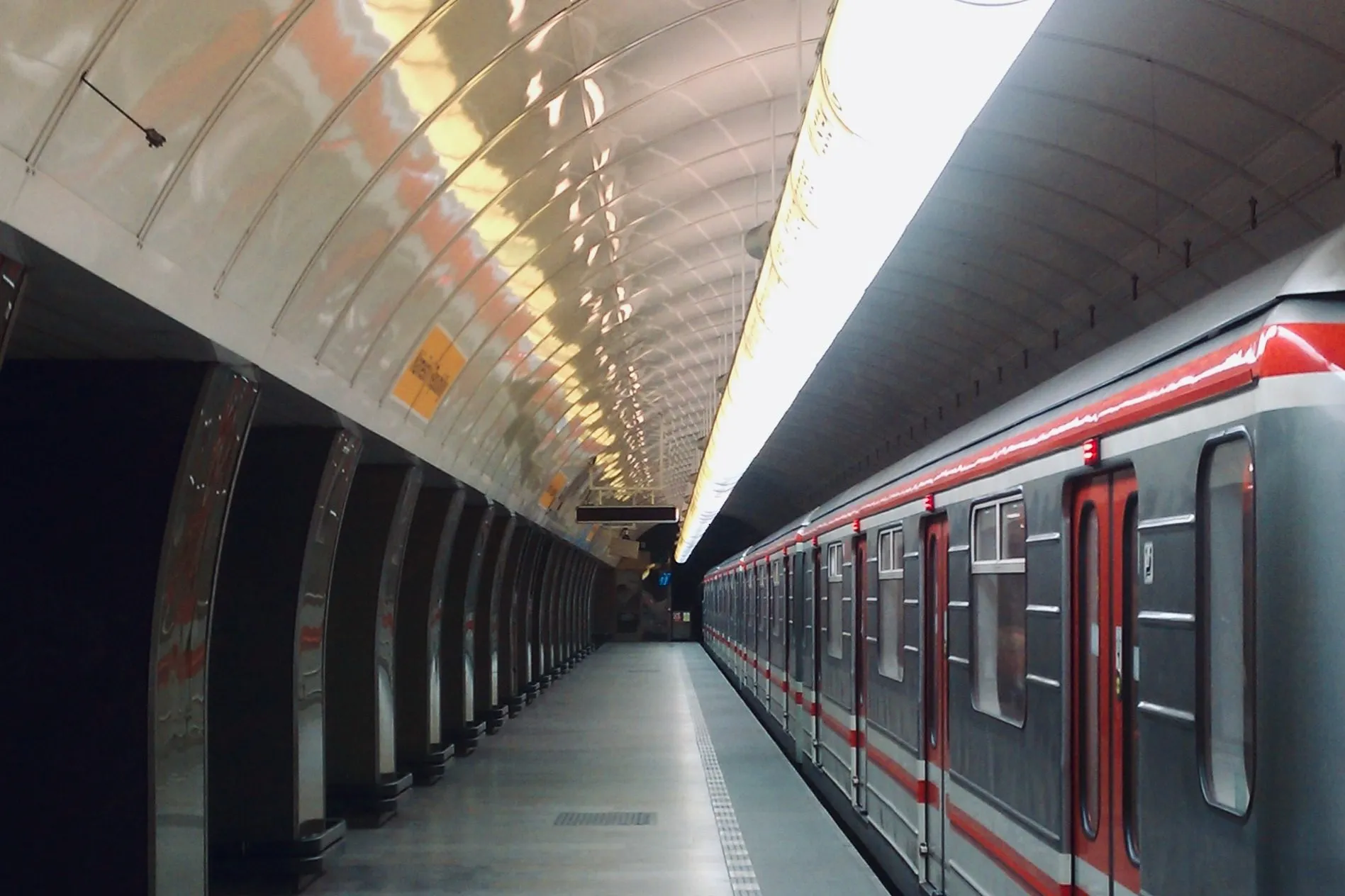 The picture shows a Prague Metro train stopping at a bright, vaulted underground platform, complementing the Prague subway map.