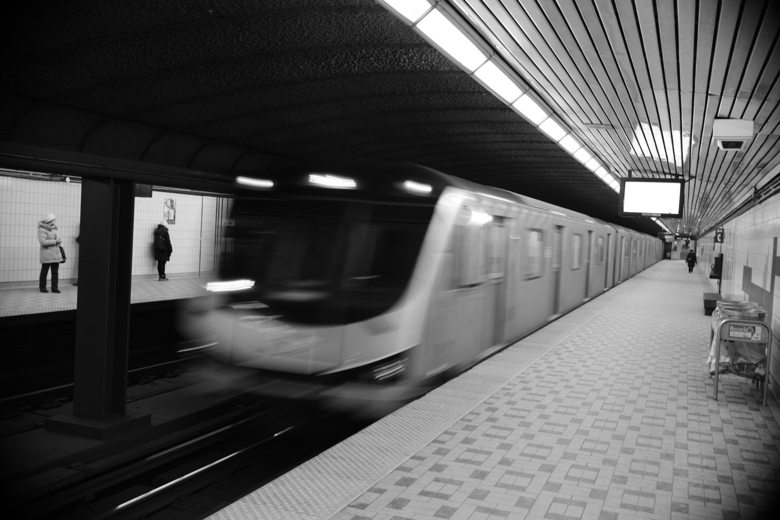 The image shows a TTC subway train arriving at a Toronto station while passengers wait on the platforms.