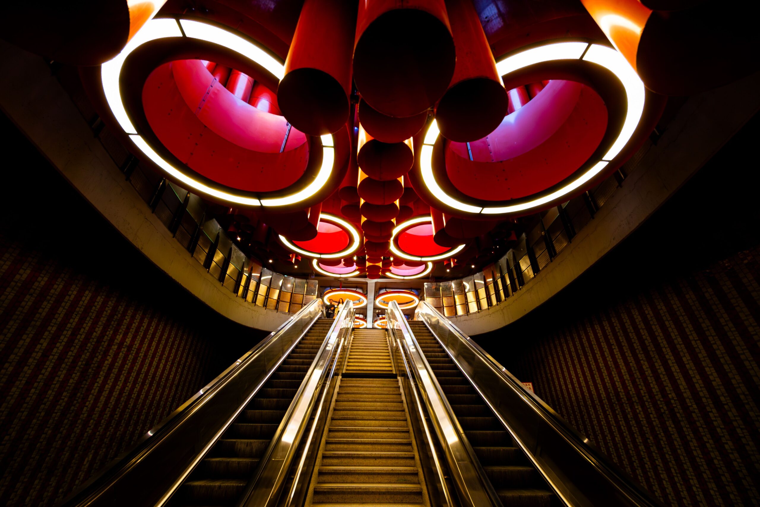 Auf dem Bild führen beleuchtete Rolltreppen durch die runde Deckenarchitektur einer Brüsseler Metrostation.