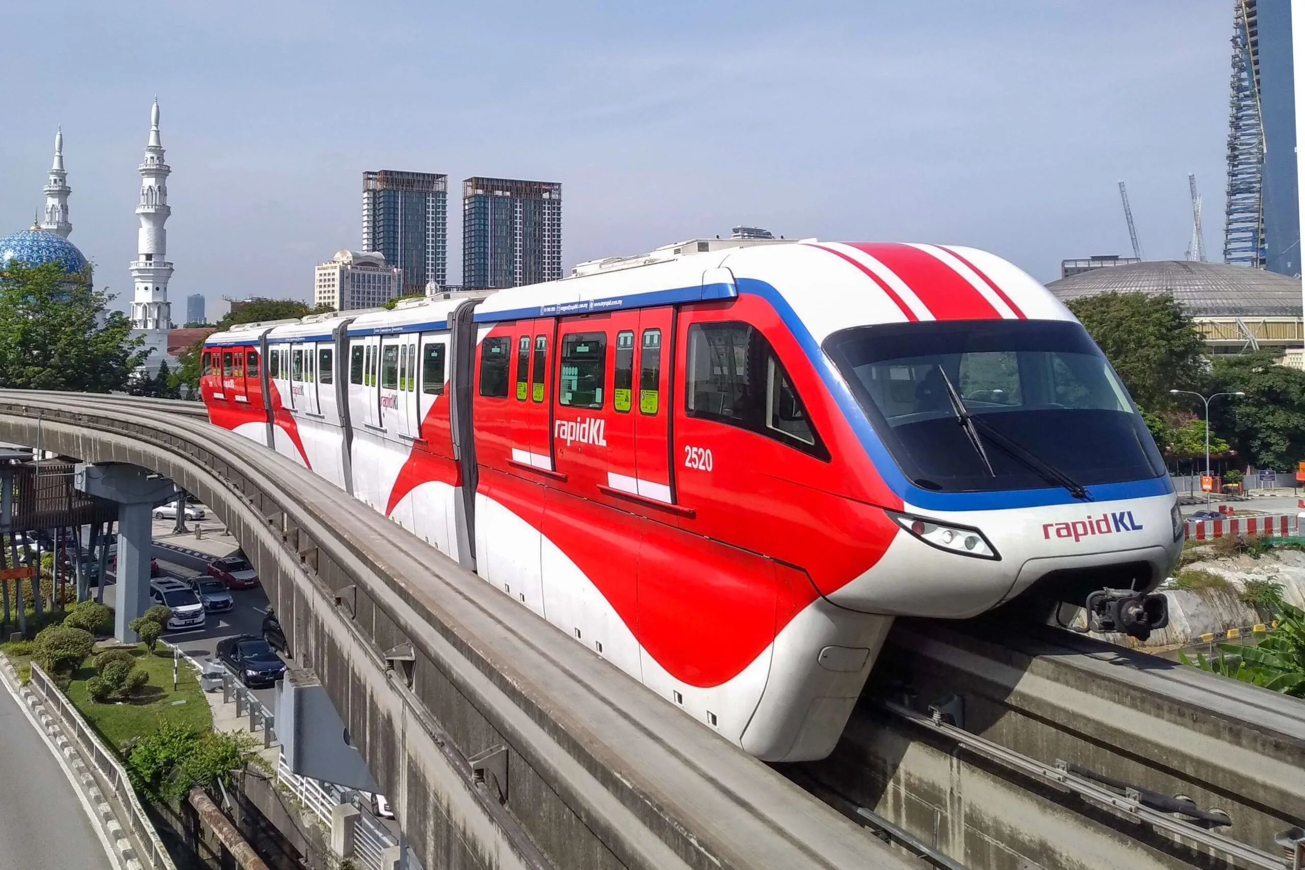 The image shows a KL Monorail train passing city landmarks on the Rapid KL network.