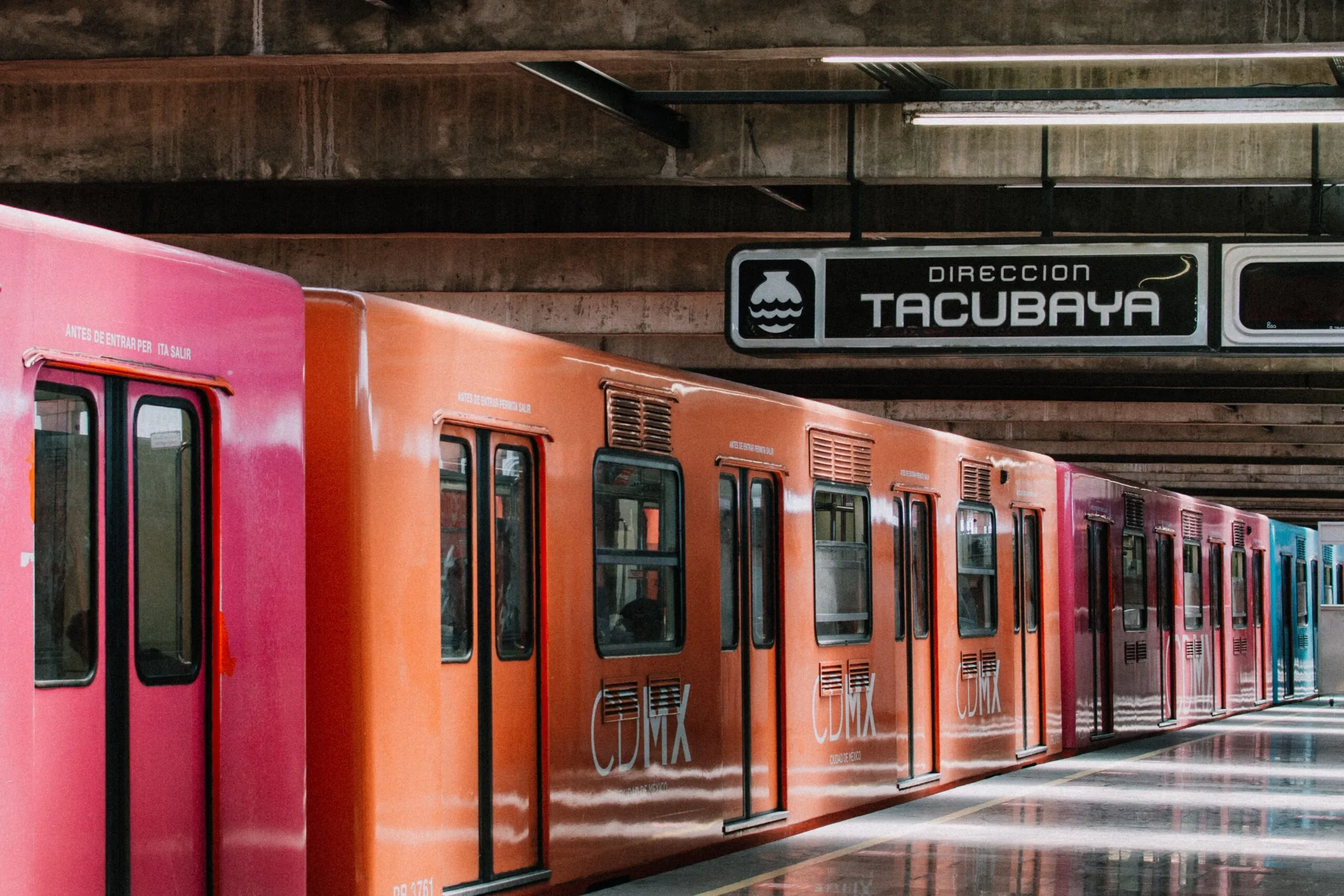 Das Bild zeigt einen orangefarbenen Zug und einen Wegweiser nach Tacubaya an der Metro Mexiko-Stadt.