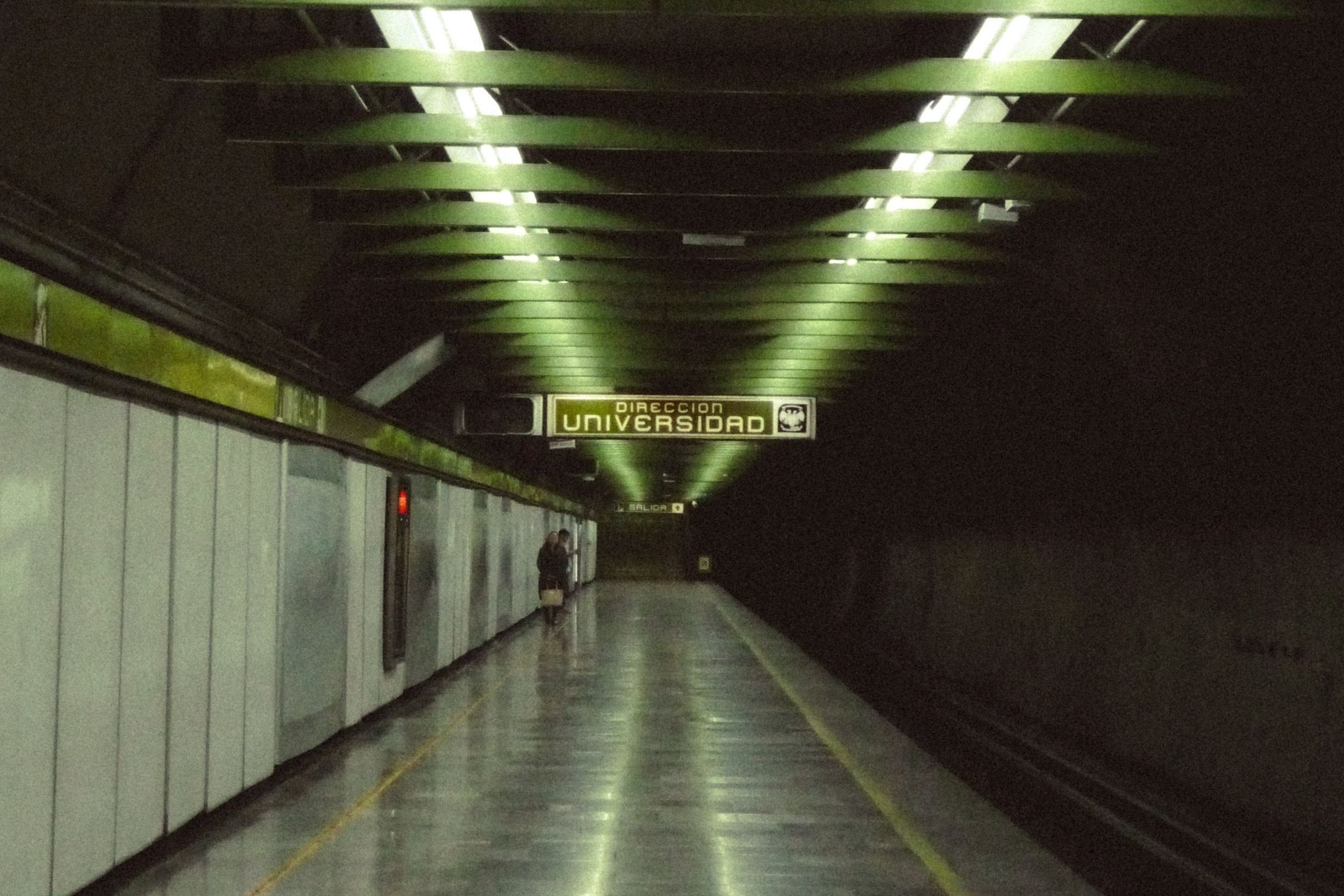 Das Bild zeigt einen Wegweiser nach Universidad und einen Fahrgast auf einem fast leeren Bahnsteig der Metro CDMX.