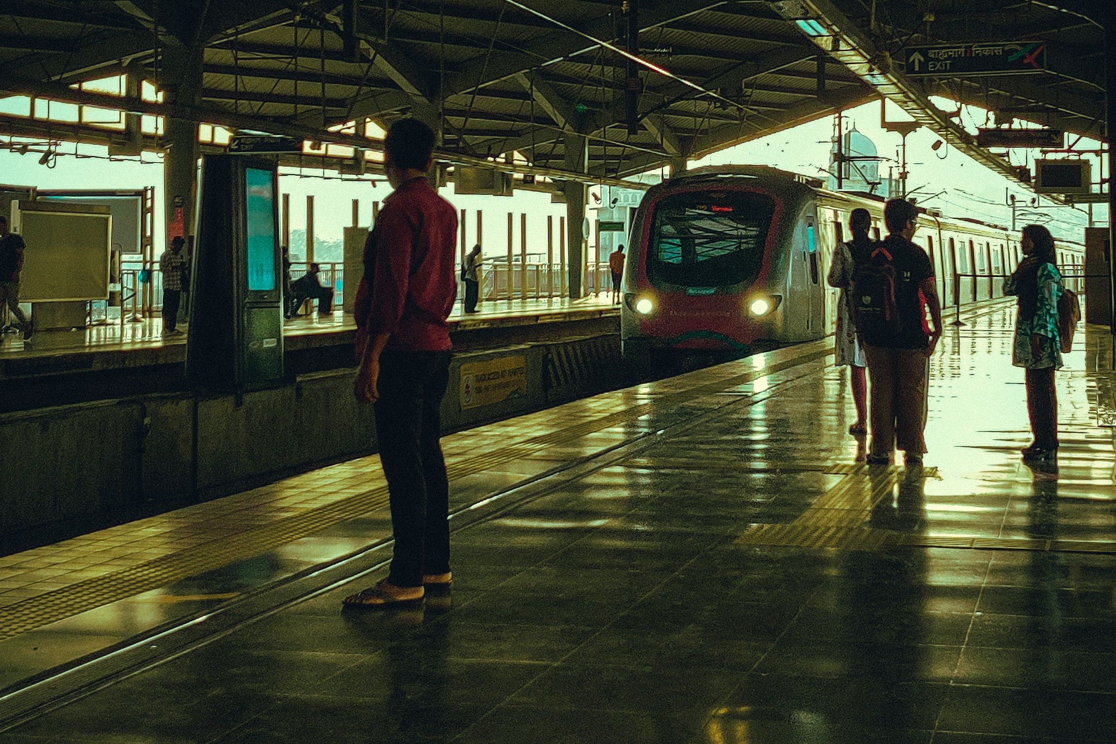 Auf dem Bild sieht man einen Zug der Metro in Mumbai, der in eine Hochbahnstation einfährt, während Fahrgäste am Bahnsteig warten.