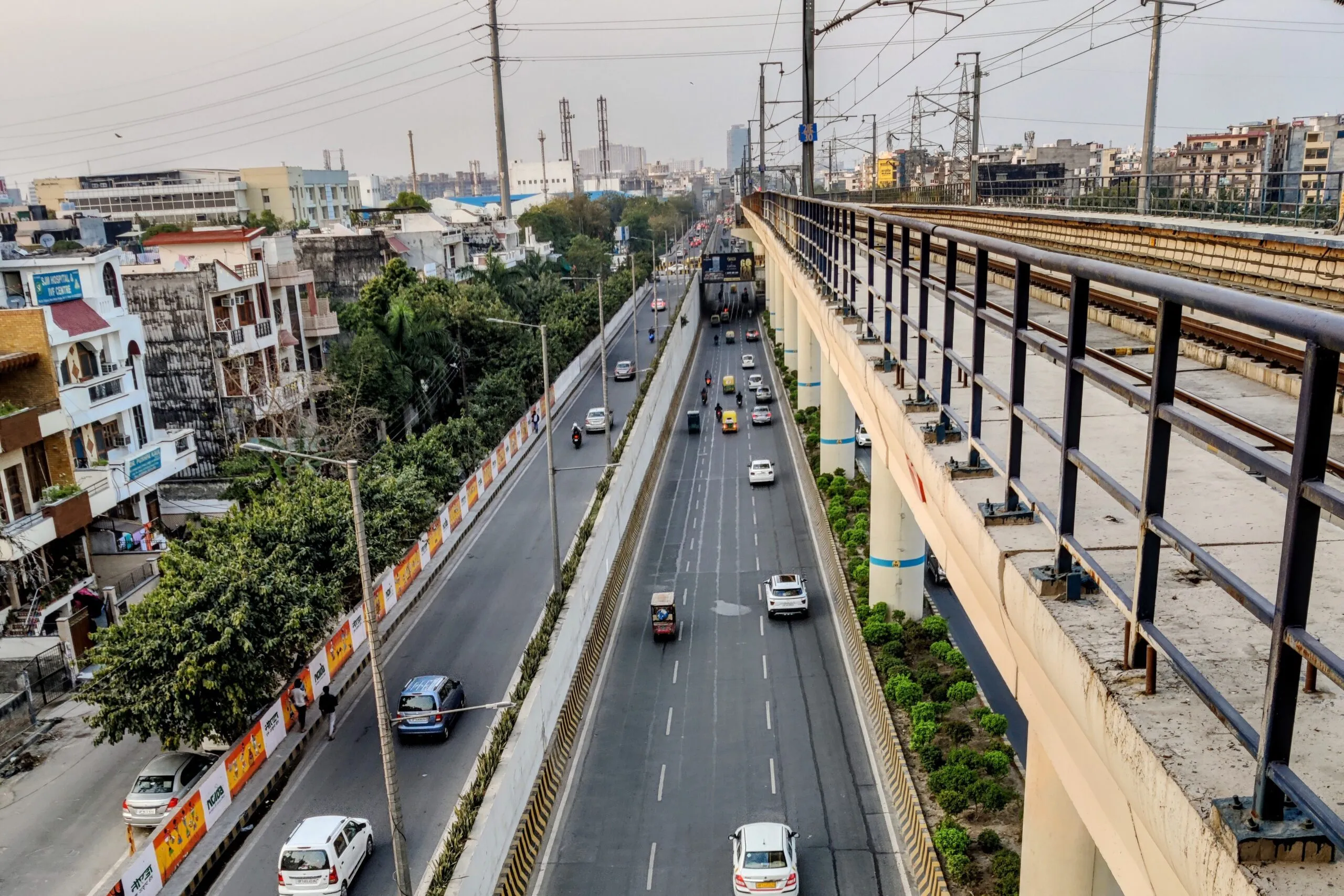 Eine erhöhte Bahntrasse verläuft in Noida neben einer mehrspurigen Straße.