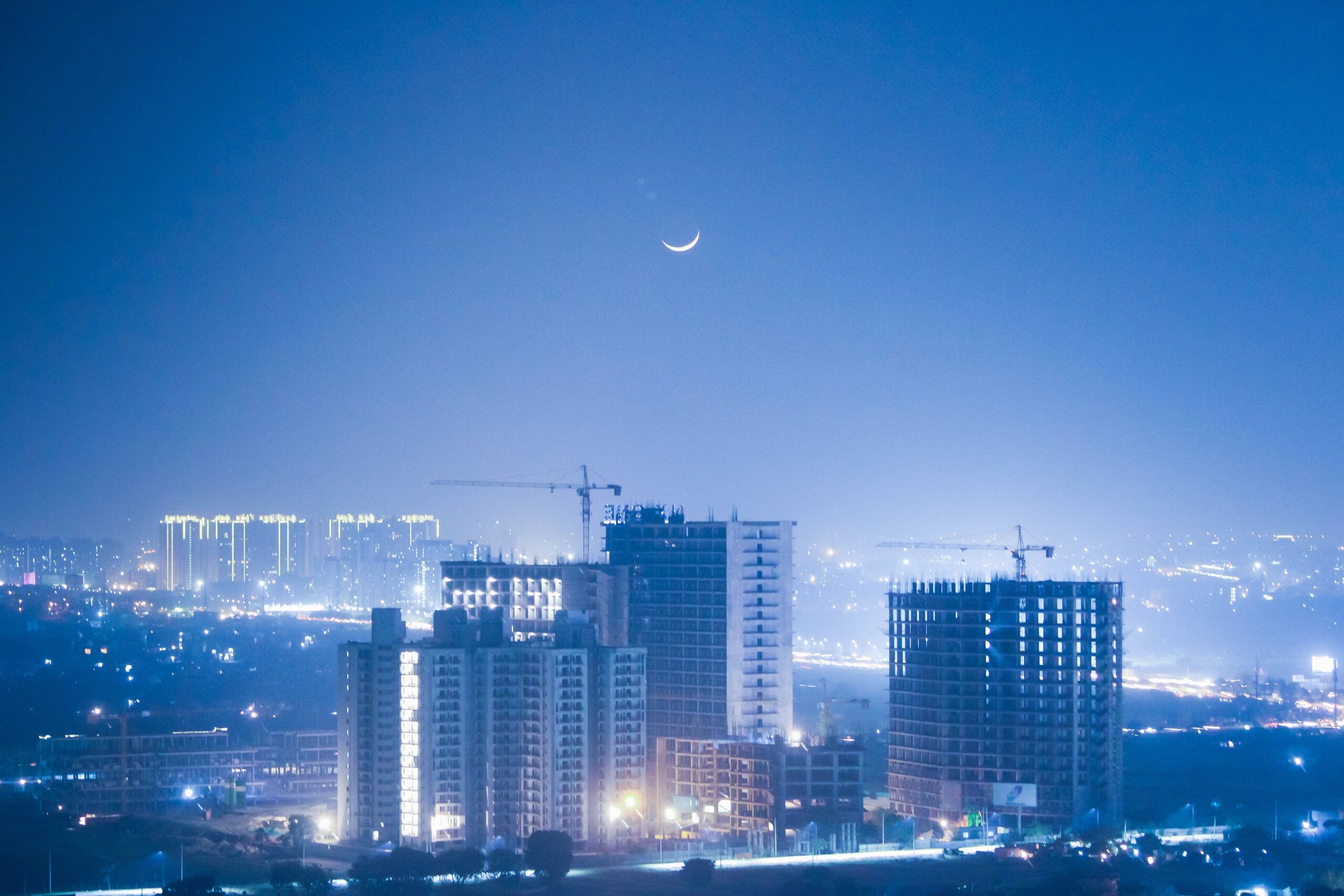 Die beleuchtete Skyline von Greater Noida erhebt sich unter einer schmalen Mondsichel.