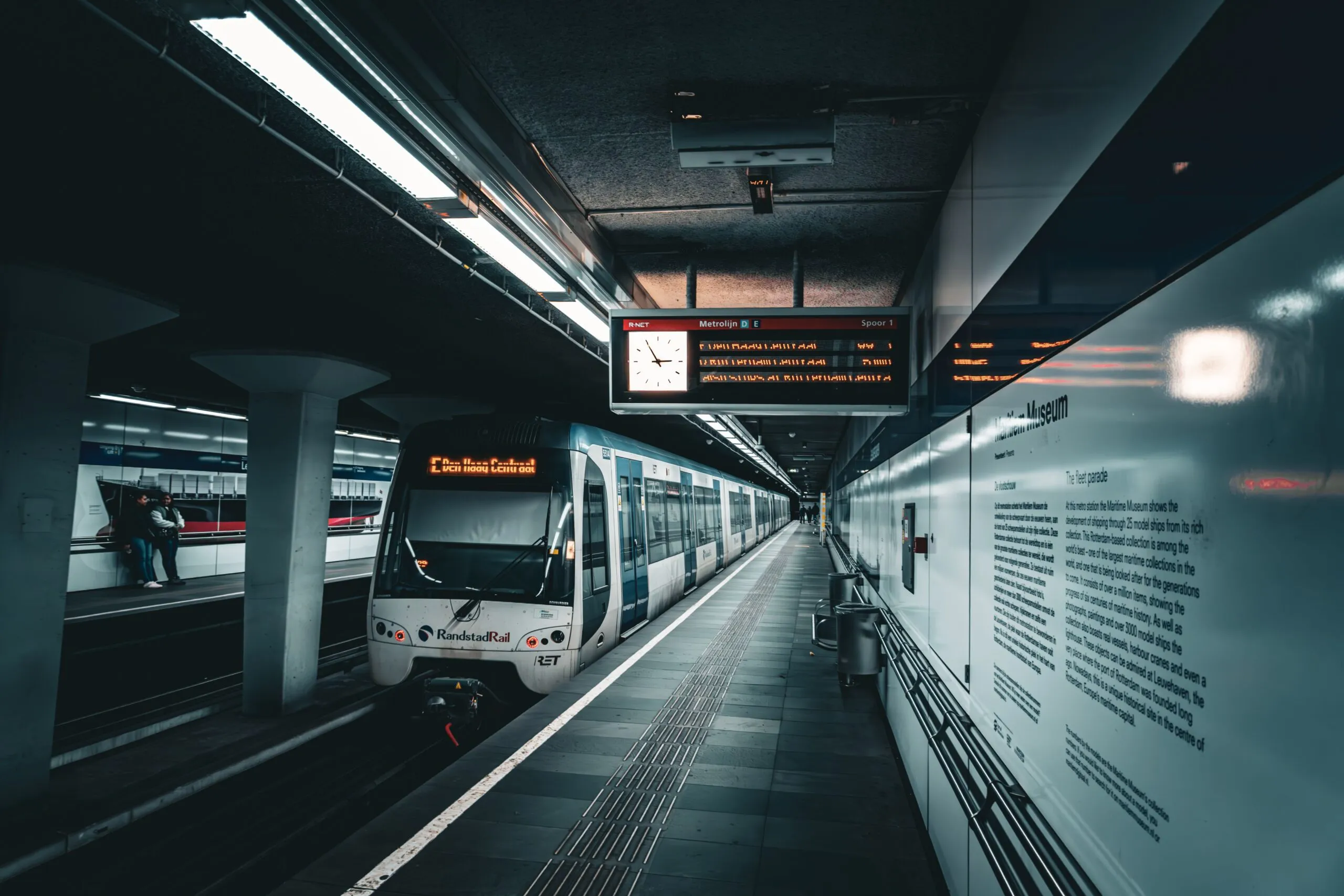 The image shows an RET RandstadRail metro train waiting at Leuvehaven station in Rotterdam.