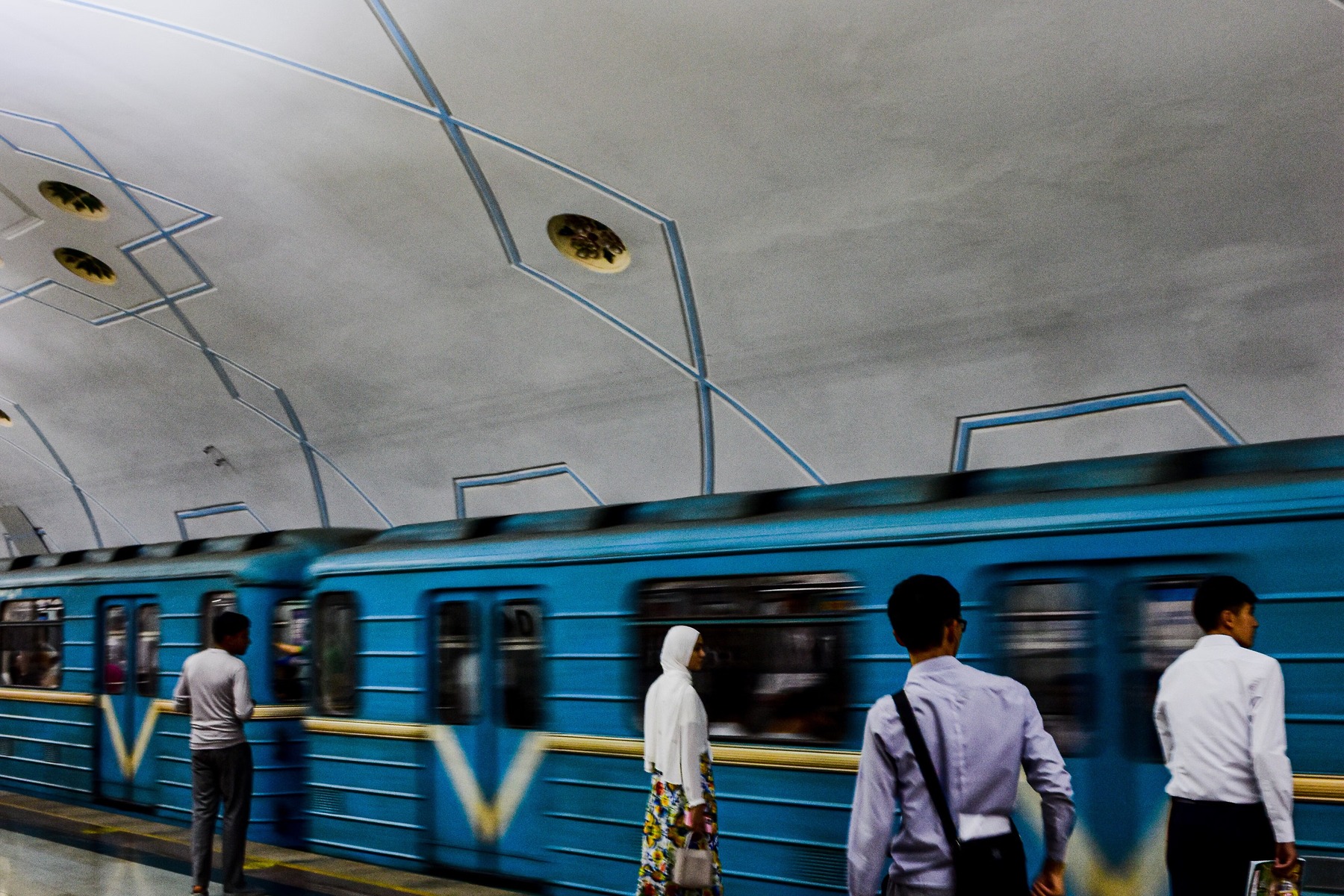 The image shows a blue Tashkent Metro train stopping at Bodomzor station while passengers wait.